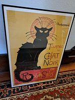 Full view of the framed Black Cat film poster leaning against a wall, showing the black cat and French text.