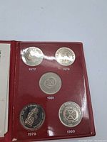 Five Canada Games tokens from 1977, 1978, 1979, 1980, 1981 in red folder showing different designs including torch and emblems