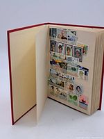 Open view of album page with vintage postage stamps affixed or mounted on transparent holders. Various subjects including portraits of historical figures, landmarks, and flora.