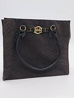 Front view of black Tommy Hilfiger handbag showing patterned fabric, black handles, and gold-tone 'TH' logo hardware on a band detail.