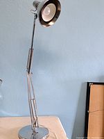 Full view of the vintage desk lamp showing the chrome adjustable arm and circular base against a light blue wall.