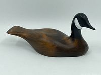 Left-side view of wooden duck decoy with dark brown body and black and white painted head.