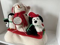 Front view showing snowman with earmuffs, red scarf, penguin and dog on red sled with white cushion base.