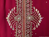 Close-up of intricate embroidery and embellishments on the front of the raspberry kaftan showing glass stones, sequins, and pearlized beads in ornate design.