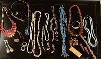 Top view showing assortment of necklaces, bracelets, earrings, pendants arranged on black background.