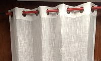 Close-up of soft white woven curtain panel hanging on red rod showing large grommet rings and fabric texture
