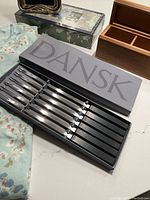 Set of eight Dansk fondue forks in original box with black handles and stainless steel prongs.
