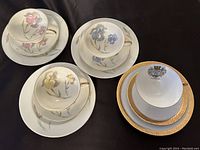 Four trio sets of luncheon plates, tea/coffee cups, and saucers displayed on black background showing floral designs on three sets and gold rim on one set