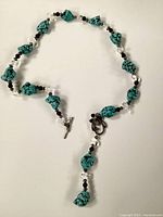 Turquoise necklace with chunky stones, black beads, glass beads, floral clasp and metal pin closure displayed flat