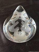 Front view of the clear crystal paperweight showing the etched abstract design with a star and signature on the base.