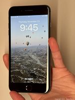 Front view of powered on iPhone 8 Plus displaying lock screen and time, held in hand.