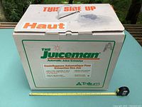 Box with 'The Juiceman Automatic Juice Extractor' printed, white box with orange and green details, measuring tape for scale.