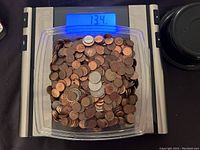 Top-down photo showing a clear plastic container filled with mixed coins on a digital scale showing 13.4 pounds.