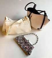 Three handbags displayed: white nylon travel bag, white textured leather handbag with brown trim, and a multicolored bejewelled evening bag.