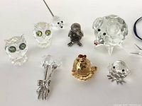 Photo showing the full set of nine Swarovski crystal pieces including owls, mouse, pig, bird, rooster, penguin, tulip brooch, and Christmas star ornament.