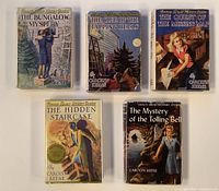 Front covers of four vintage Nancy Drew books with dust jackets showing wear. Titles visible and cover illustrations in mid-20th century style.