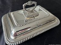 Top side angle view of the vintage Regis silver plated covered dish showing the rectangular lid with ornate heart-shaped handle and decorative rope edge.