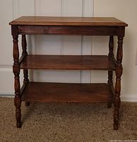 Front view of 3 tier wooden side table showing three shelves and turned legs.
