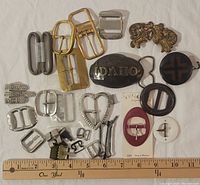 Top-down image showing full lot assortment of belt buckles and money clip for scale, with a ruler for size reference.