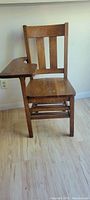 Vintage wooden school desk chair with built-in writing surface seen on a light wood floor.