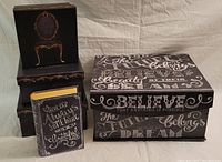 Photo showing all three black decorative boxes with white text and motifs arranged on a surface.