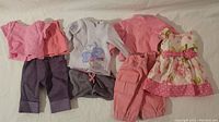 Various doll clothes for American Girl and same size dolls including shirts, pants, dress, hat, skirt, and boots