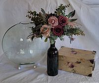 Photo of dark glass vase holding artificial bridesmaid bouquet with roses and greenery, beside a matching floral decorative box.