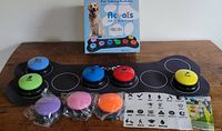 Pet talking buttons mounted on a black base with multi colored circular buttons, some with stickers and batteries installed, others unused.