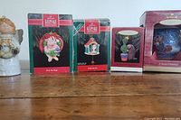 Four Hallmark Keepsake Ornament boxes arranged on a wooden surface, showing box art for Deck the Hogs, New Home house, Strange but Wonderful Relationship cactus and beaver, and one other box.