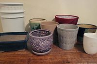 Front view of various ceramic and plastic plant pots of different colors and designs on wooden table.