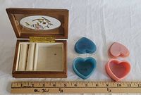 Rectangular wooden jewelry box open showing inside compartments, next to two open heart-shaped jewelry boxes in blue and pink.