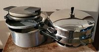 Electric waffle maker and electric pressure cooker side by side, metal polished finish, black handles on lids.