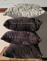 Four decorative throw pillows stacked against a wall showing different colors and textures