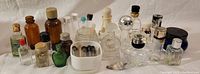 Varied perfume and make-up bottles on a flat surface showing assortment of shapes, sizes, and colors including amber, green, clear, and silver accents