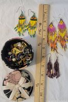 Three pairs of handmade beaded earrings displayed alongside a decorative fabric-covered box containing assorted jewelry items including post earrings.
