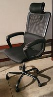 Side angled view of black office chair showing mesh backrest, headrest, armrest, and wheeled base