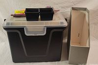 Black plastic file box with a clasped translucent lid and a neutral colored magazine file holder next to it.