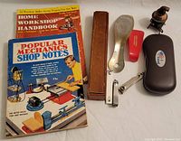 Vintage home workshop handbooks, metal shoehorn with leather case, mechanical pencil sharpener, red nail clipper, eyeglasses case with glasses