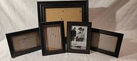 Set of one 8x10 black picture frame and four 4x6 black picture frames arranged on a beige surface.