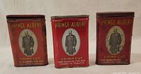 Front view showing three vintage Prince Albert Crimp Cut tobacco tins with red background and gentleman portrait.