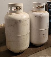 Side view of two white propane tanks, showing wear and valve fittings.