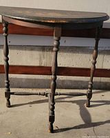 Small half oval wooden table showing front and legs, worn dark wood finish