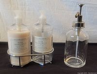 Williams Sonoma Pink Grapefruit hand soap and lotion bottles in black metal caddy, next to a separate clear glass soap dispenser with silver metal pump.