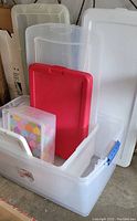 Clear plastic storage boxes with white and red lids, one large box open showing smaller box with colorful heart design inside.