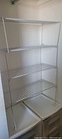 Single white metal wire shelf unit with four tiers shown empty against a white wall.
