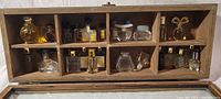 Single wooden display case with 12 compartments containing 12 tiny perfume bottles of various shapes and sizes.