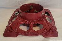 Top angled side view of the red iron Christmas tree stand showing decorative embossed patterns and the tightening screws inside the ring.