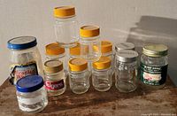 Photo showing all 12 vintage glass jars grouped together, some with branded lids such as Folgers, Miracle Whip, Heinz, and Master Store Provisions.