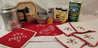 Photo of vintage kitchen items including red hotpad with embroidered initials, assorted napkins, metal canister, coffee pot figurine, decorative box, and spice containers arranged on a table.
