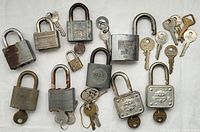 Full lot of 11 vintage padlocks with assorted keys laid out on white background.